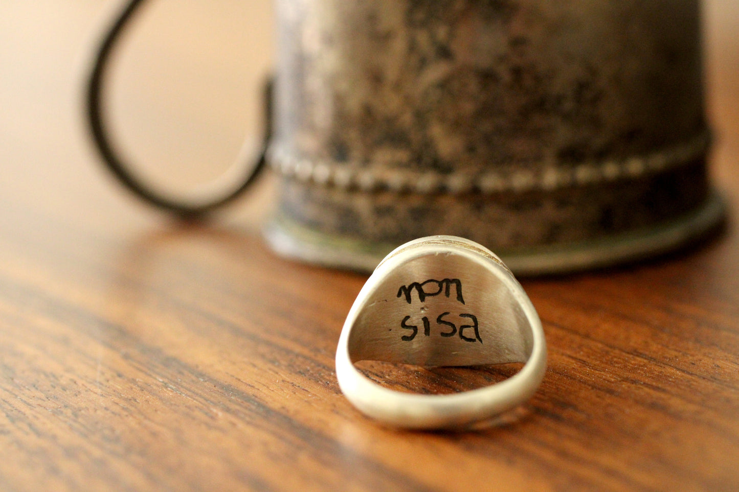 Close-up of a silver ring engraving on a wooden surface with a blurred background
