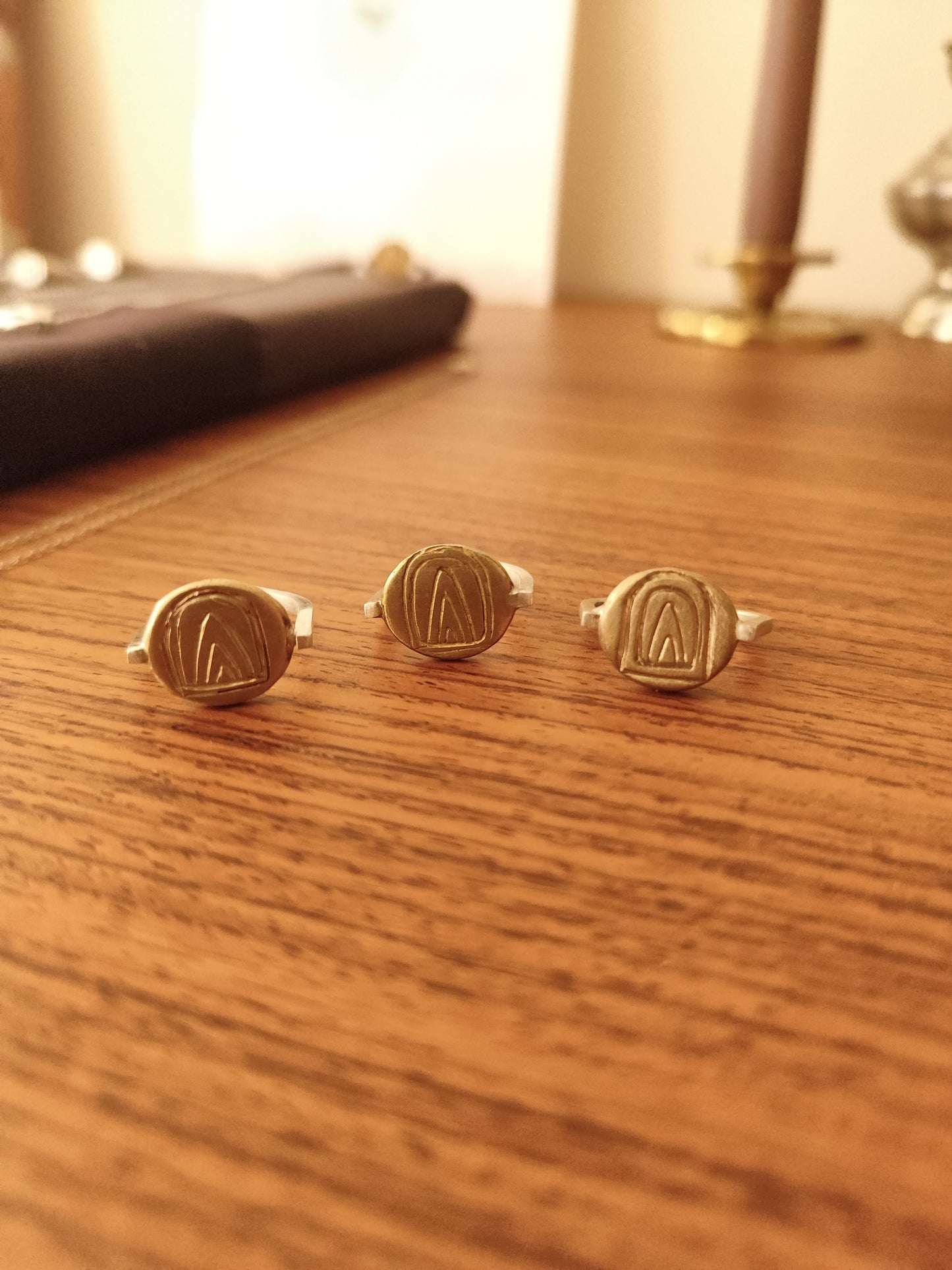 Three signet rings with engraved geometric mountain designs, arranged on a wooden tabletop.