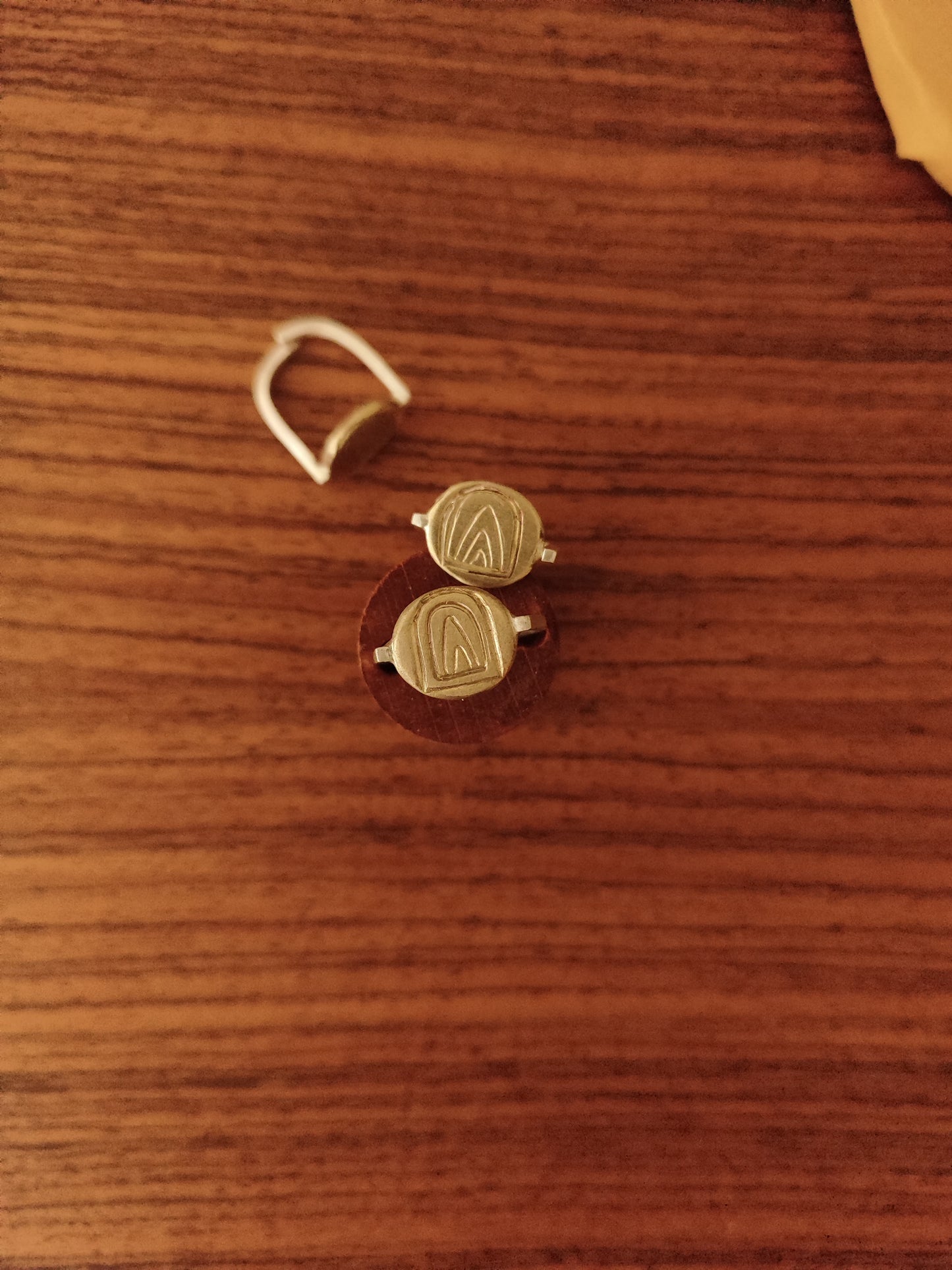 A pair of gold-toned bronze and silver engraved rings with a mountain design face and a matching ring, displayed on a brown wooden surface.