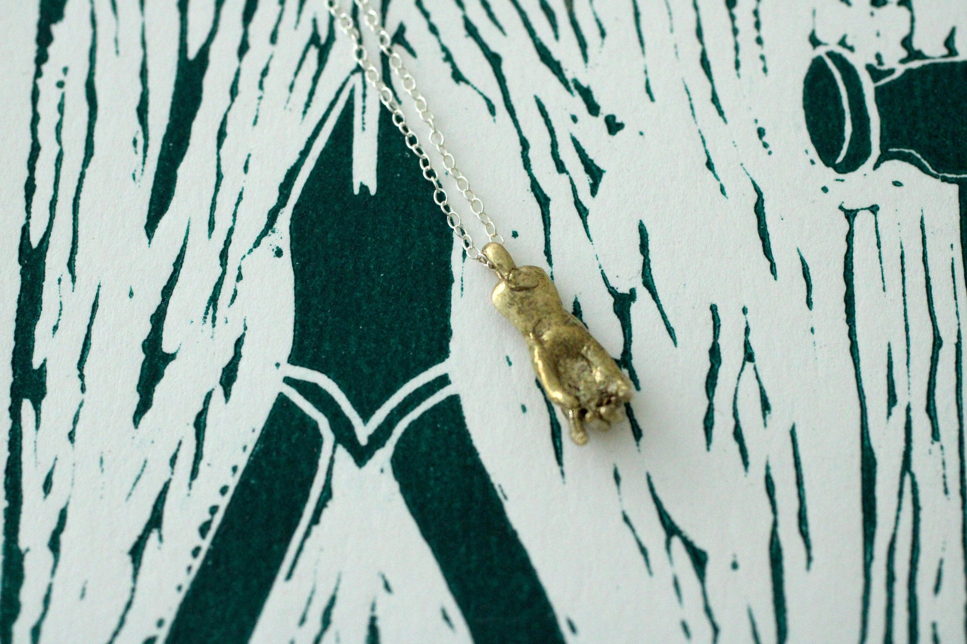 Bronze hand shape pendant on a silver chain against a patterned background