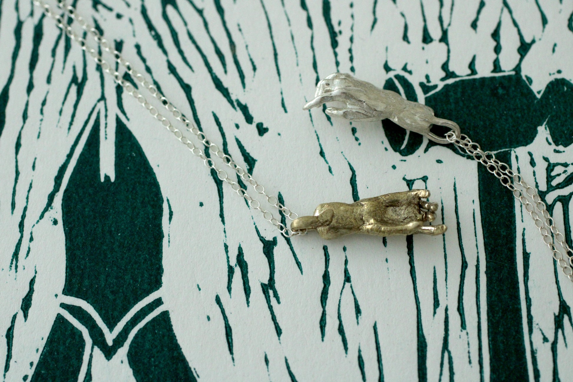 Two necklaces with a silver and bronze pendant on a white and green patterned background