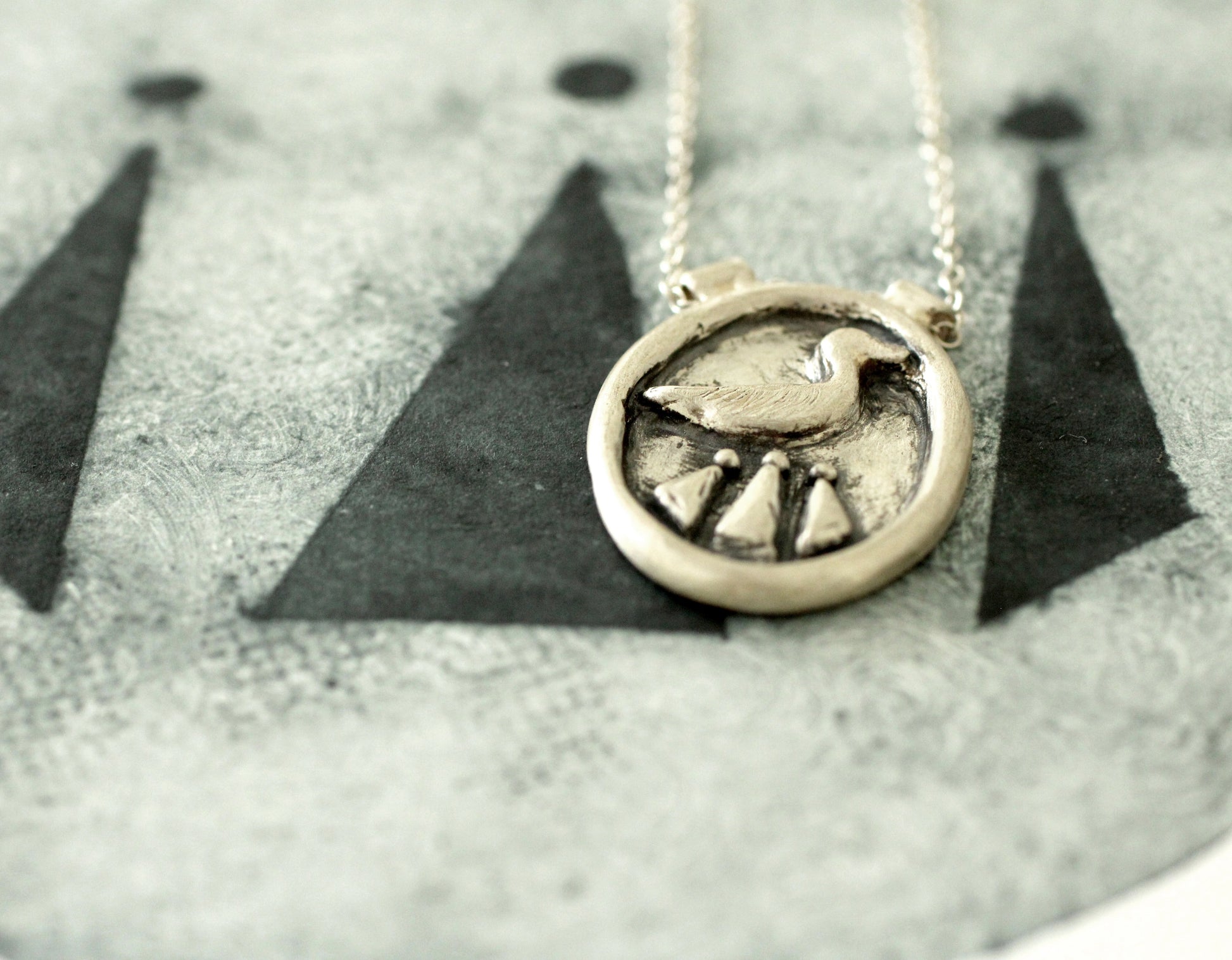 Silver necklace with a circular pendant featuring a duck and celtic design on a textured surface.