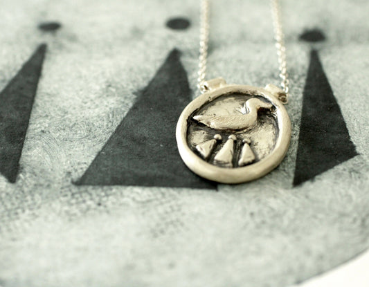 Silver necklace with a circular pendant featuring a duck and celtic design on a textured surface.