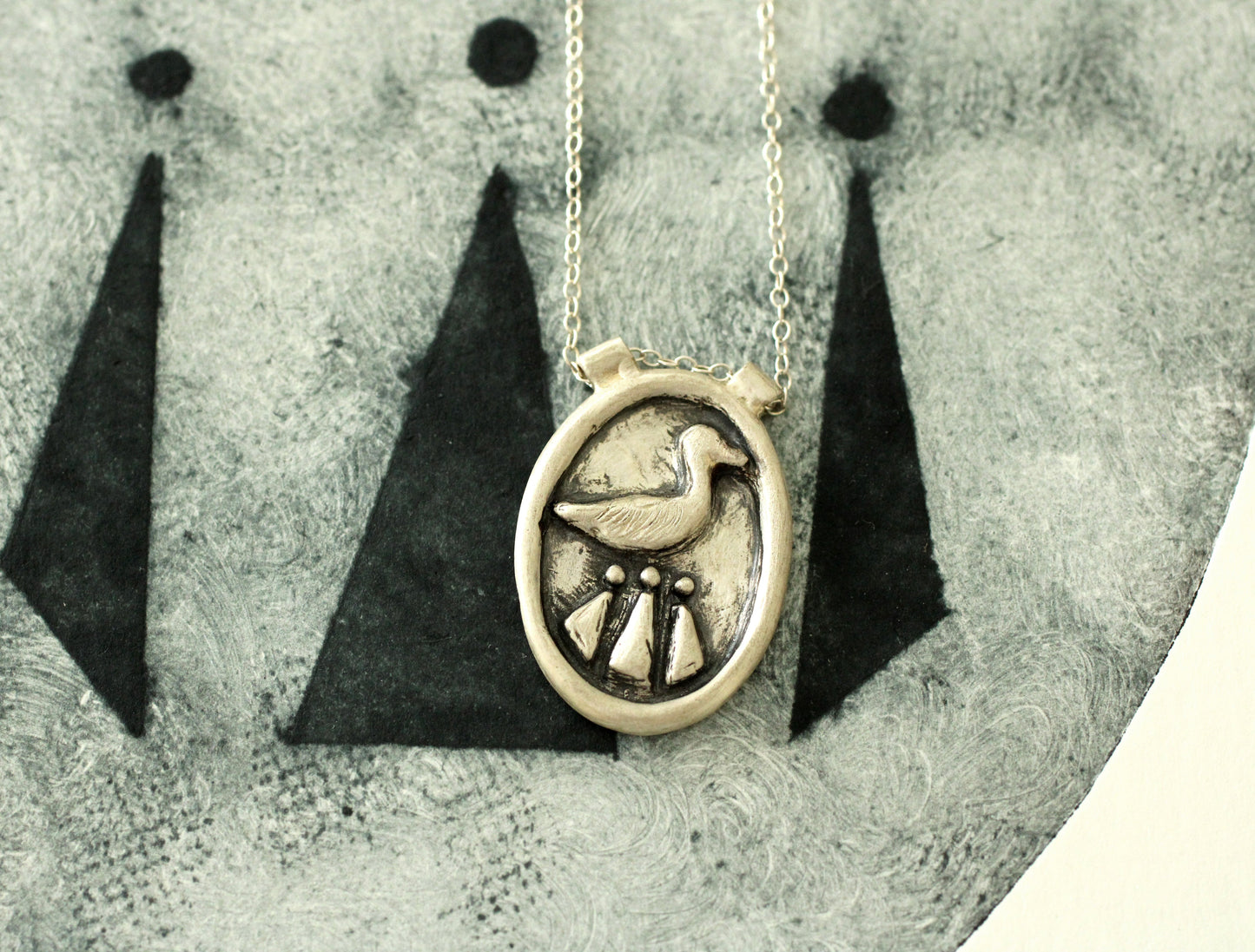 Silver necklace with a circular pendant featuring a duck and celtic design on a textured surface.