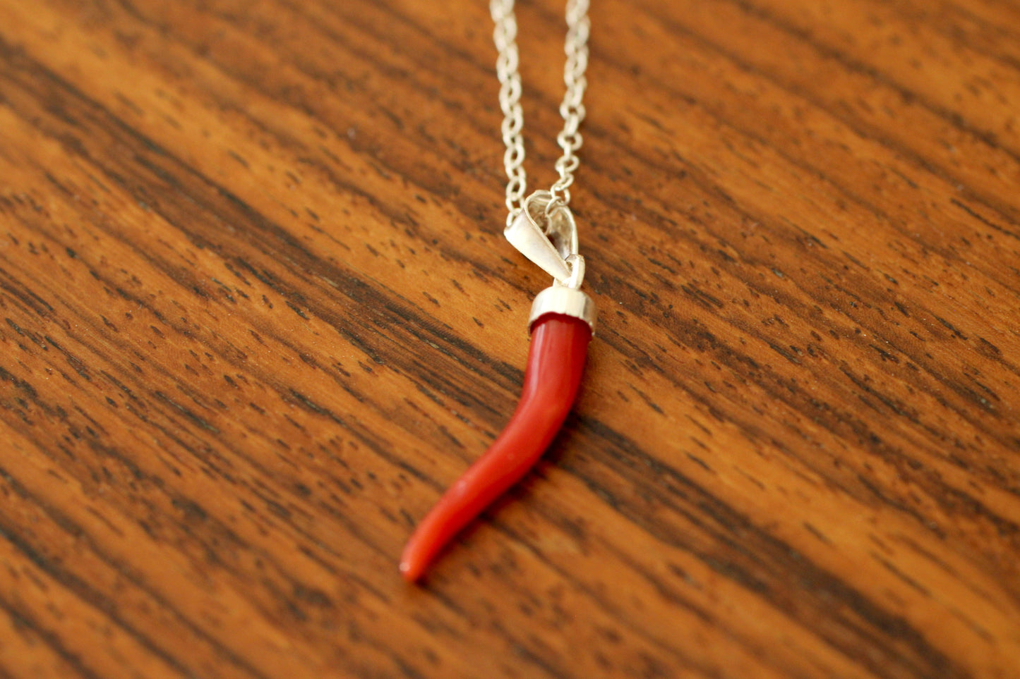 Red coral pendant on a silver chain against a wooden background