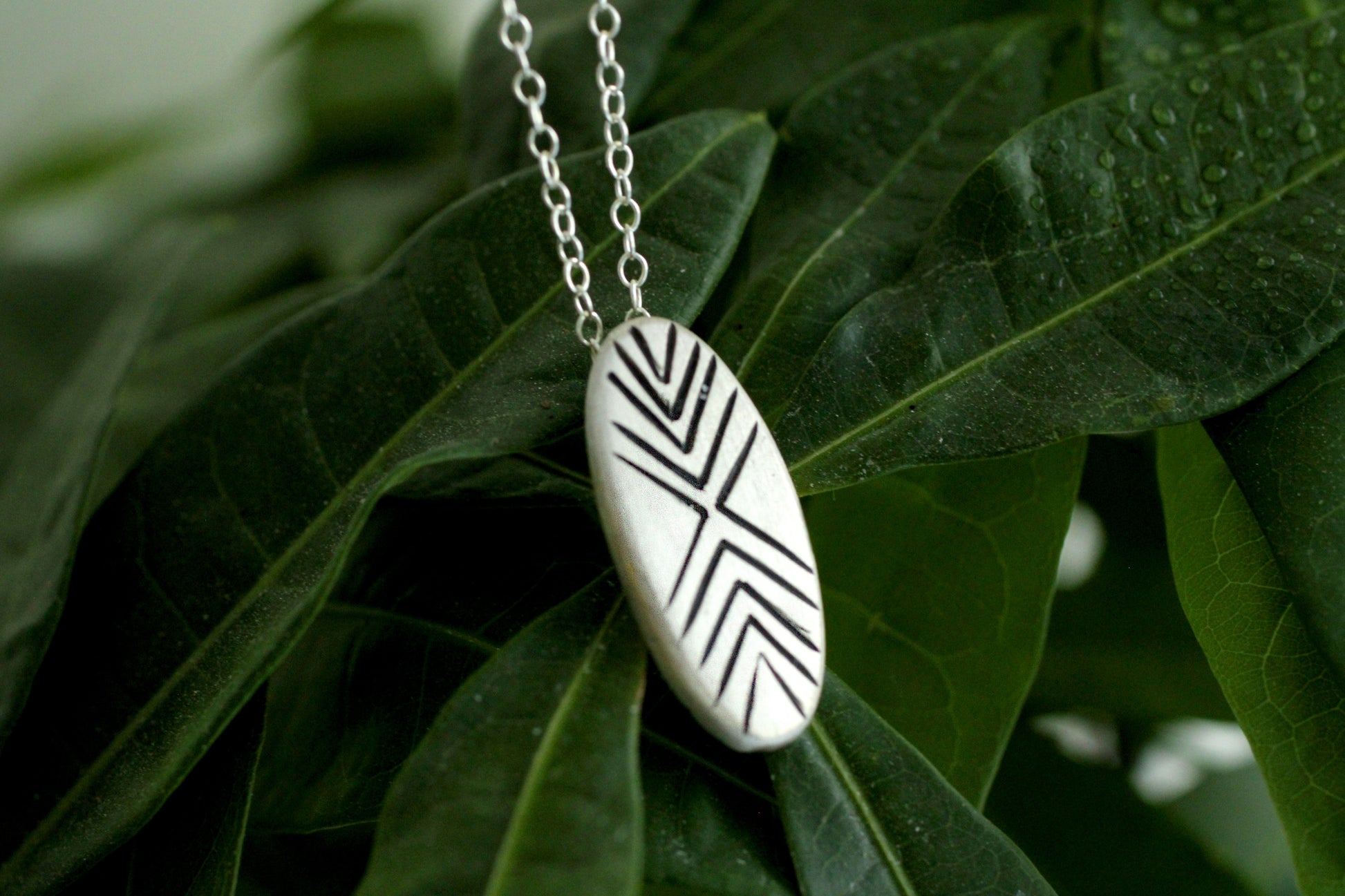 Necklace with a silver pendant with black geometric patterns engraved on green leaves
