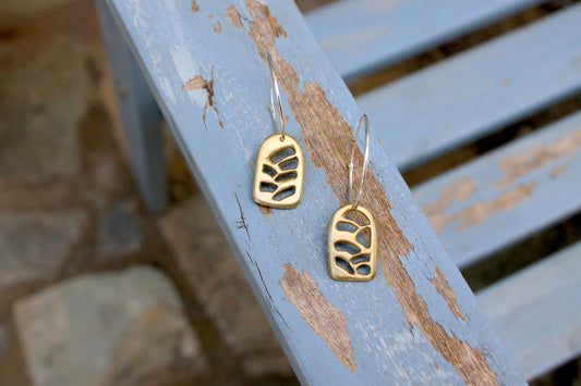 A pair of bronze earrings with silver hoops, featuring a geometric pattern, displayed on a wooden surface.