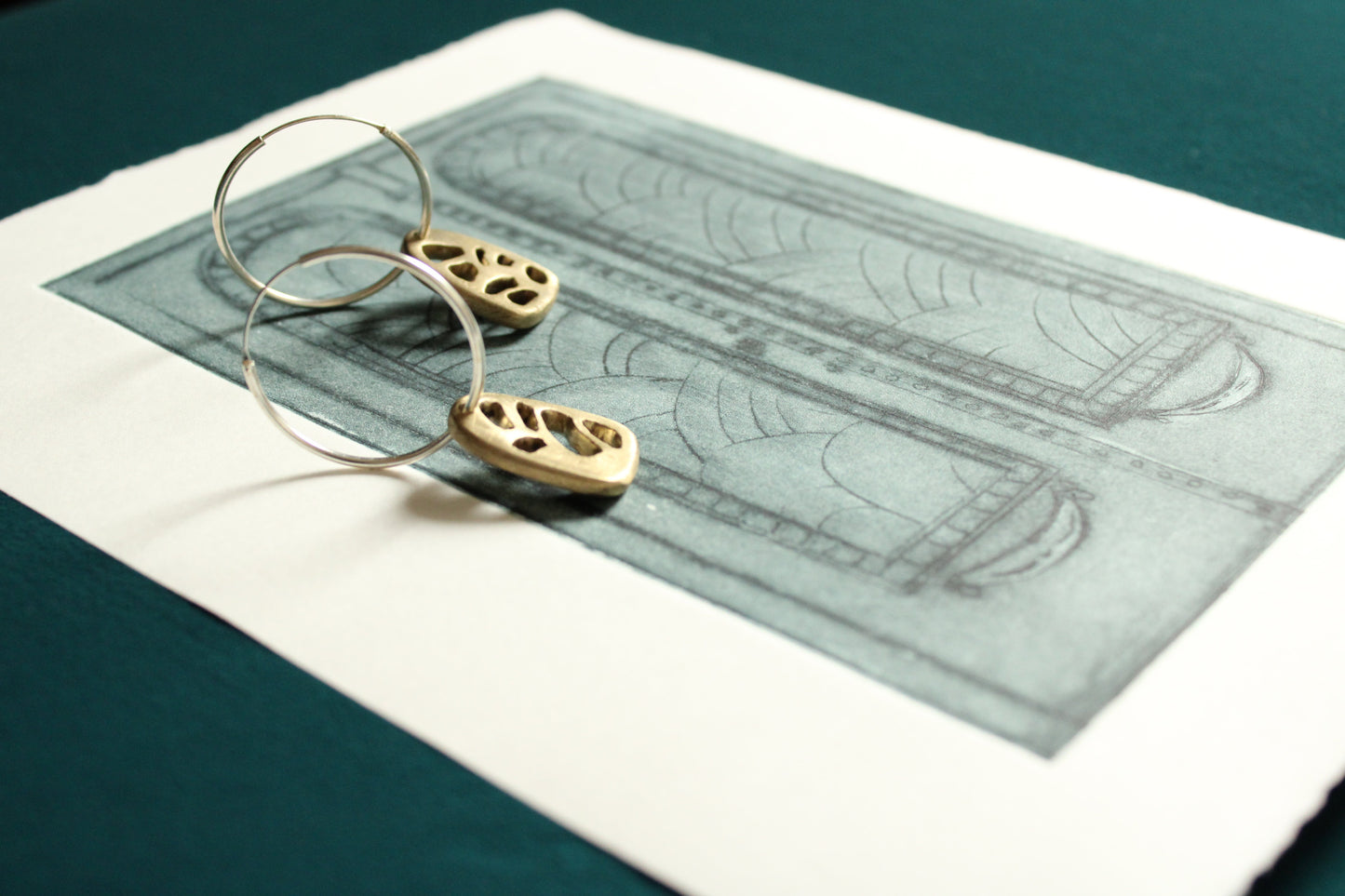 A pair of bronze earrings with silver hoops, featuring a geometric pattern, displayed on a print illustration of a door. 