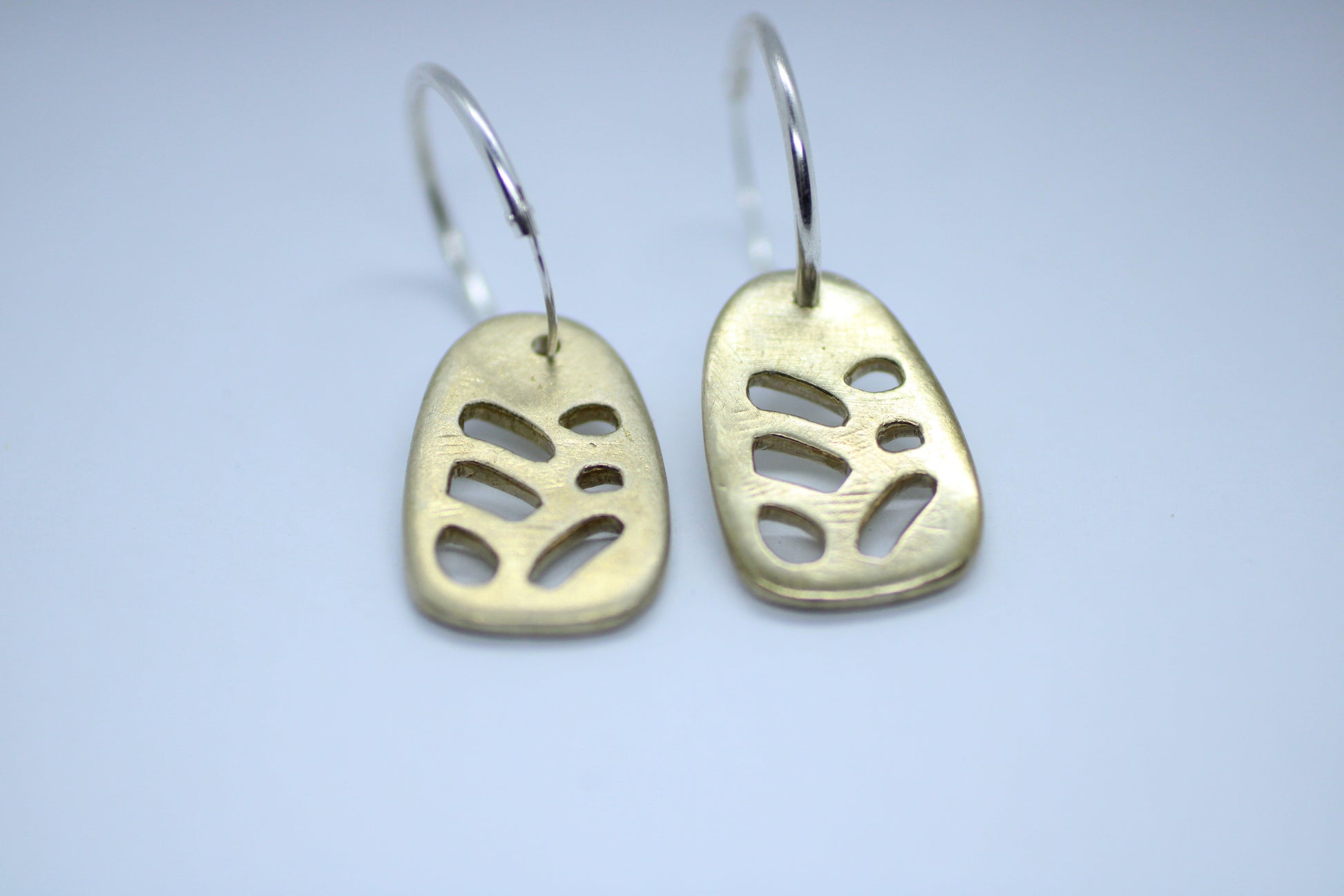 A pair of bronze earrings with silver hoops, featuring a geometric pattern, displayed on a white surface.