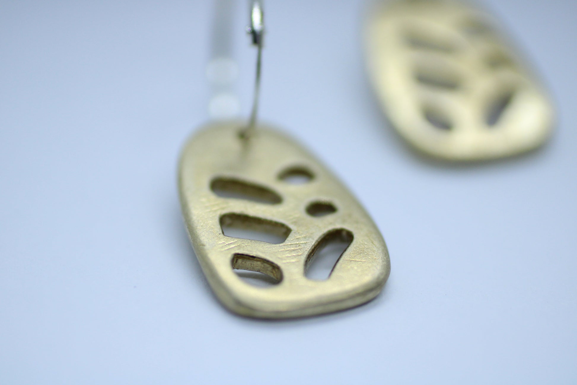 A pair of bronze earrings with silver hoops, featuring a geometric pattern, displayed on a white surface.