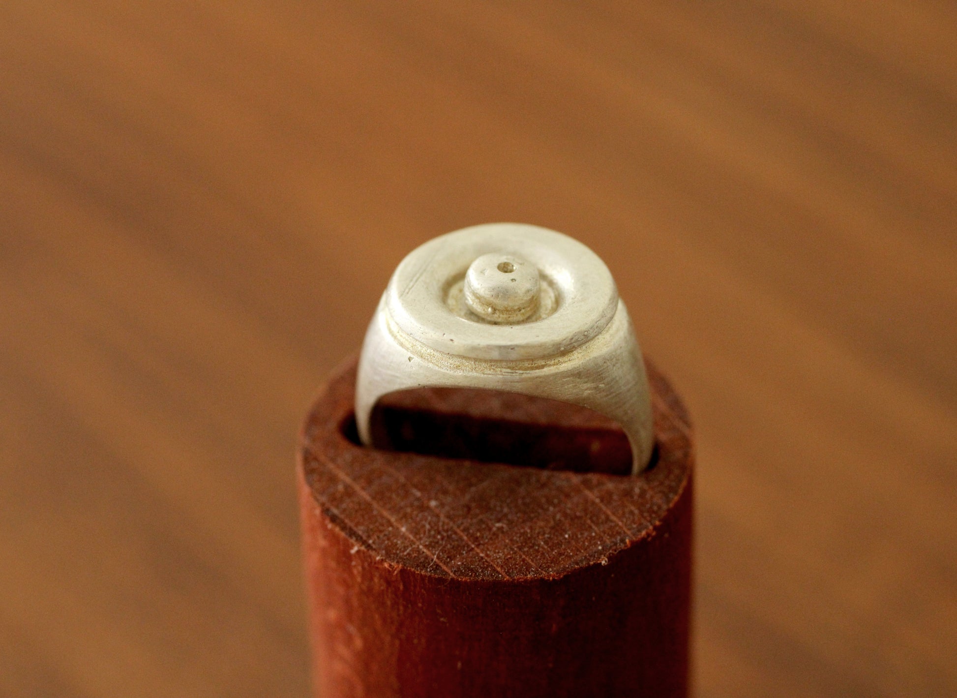 Close-up of a silver ring with a ball shape in the center on a brown surface