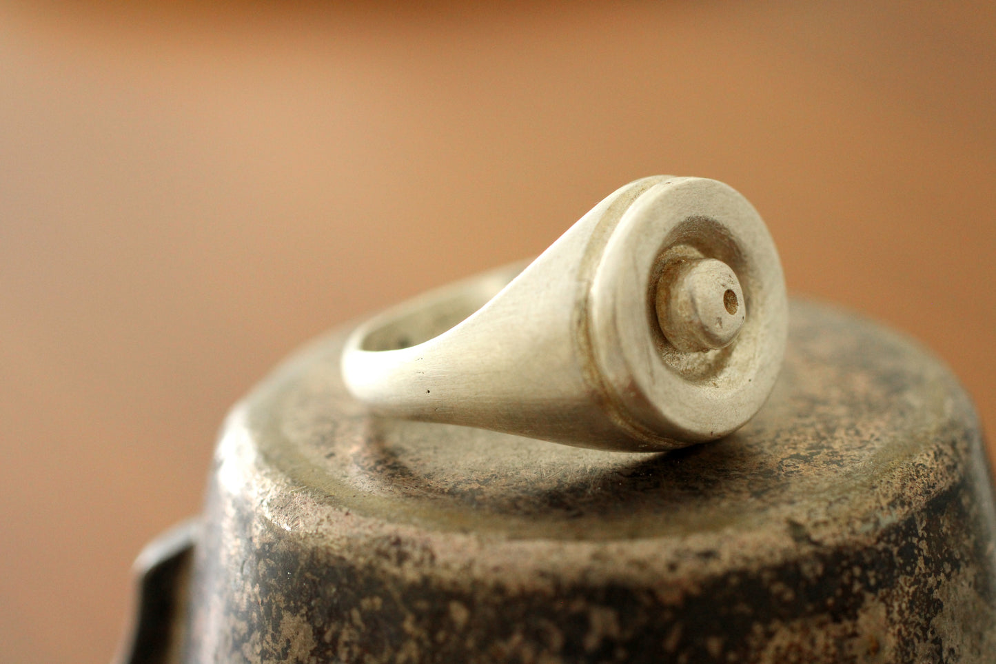 Close-up of a silver ring with a ball shape in the center on a brown surface
