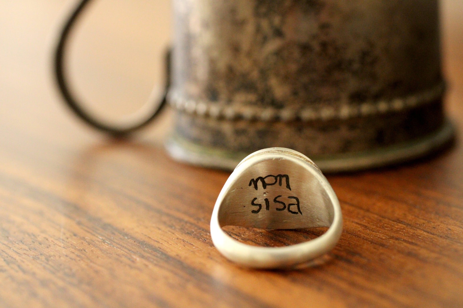 Close-up of a silver ring engraving on a wooden surface with a blurred background