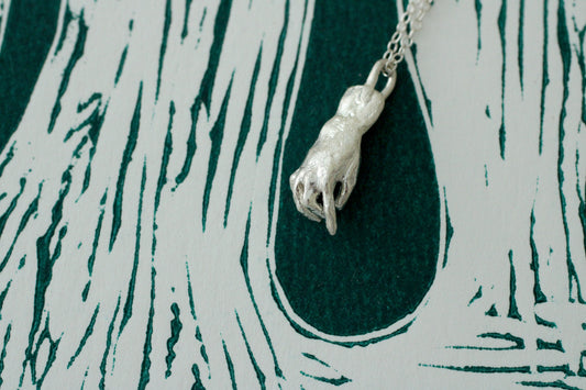 Silver hand pendant on a chain against a textured green and white background
