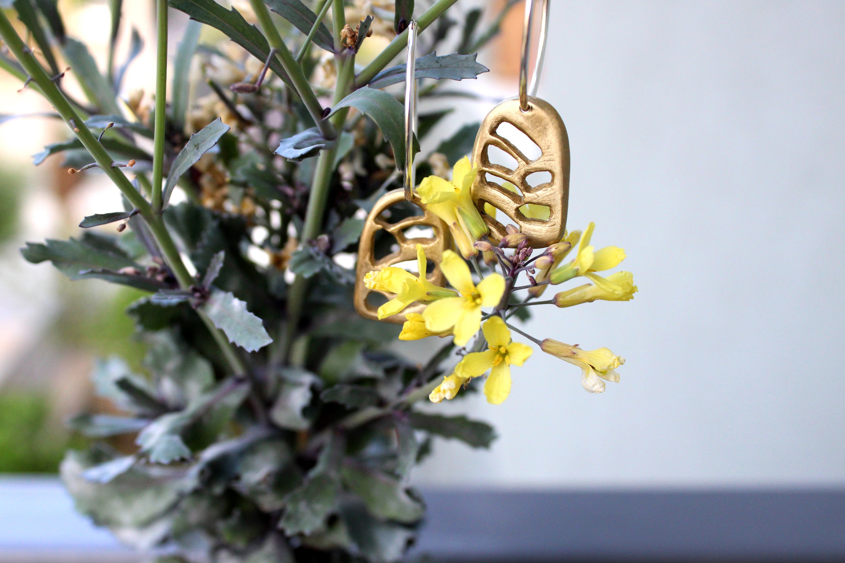 Close-up of two bronze earrings hanging from a plant