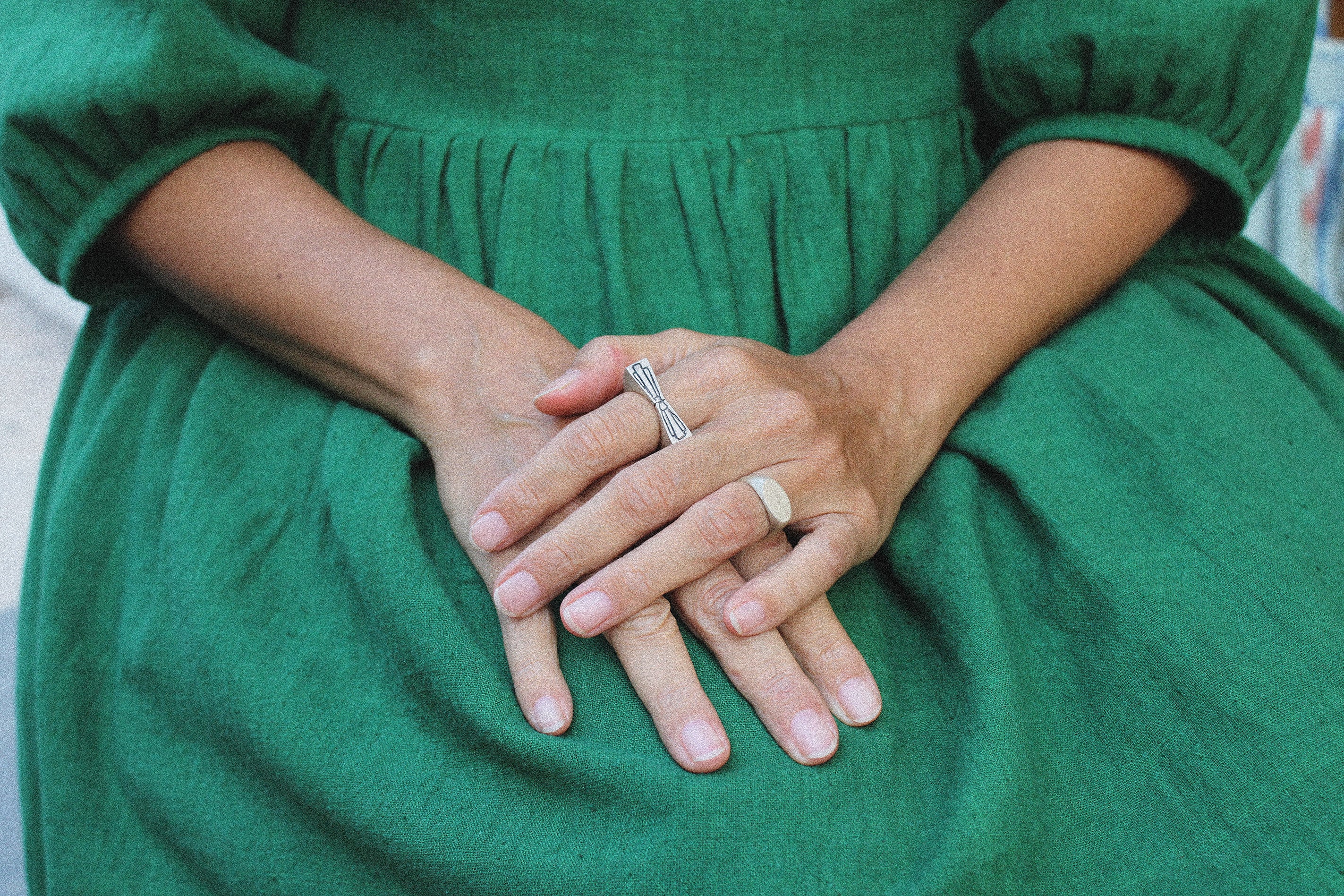 Person in a green dress with hands clasped together wearing two silver rings 