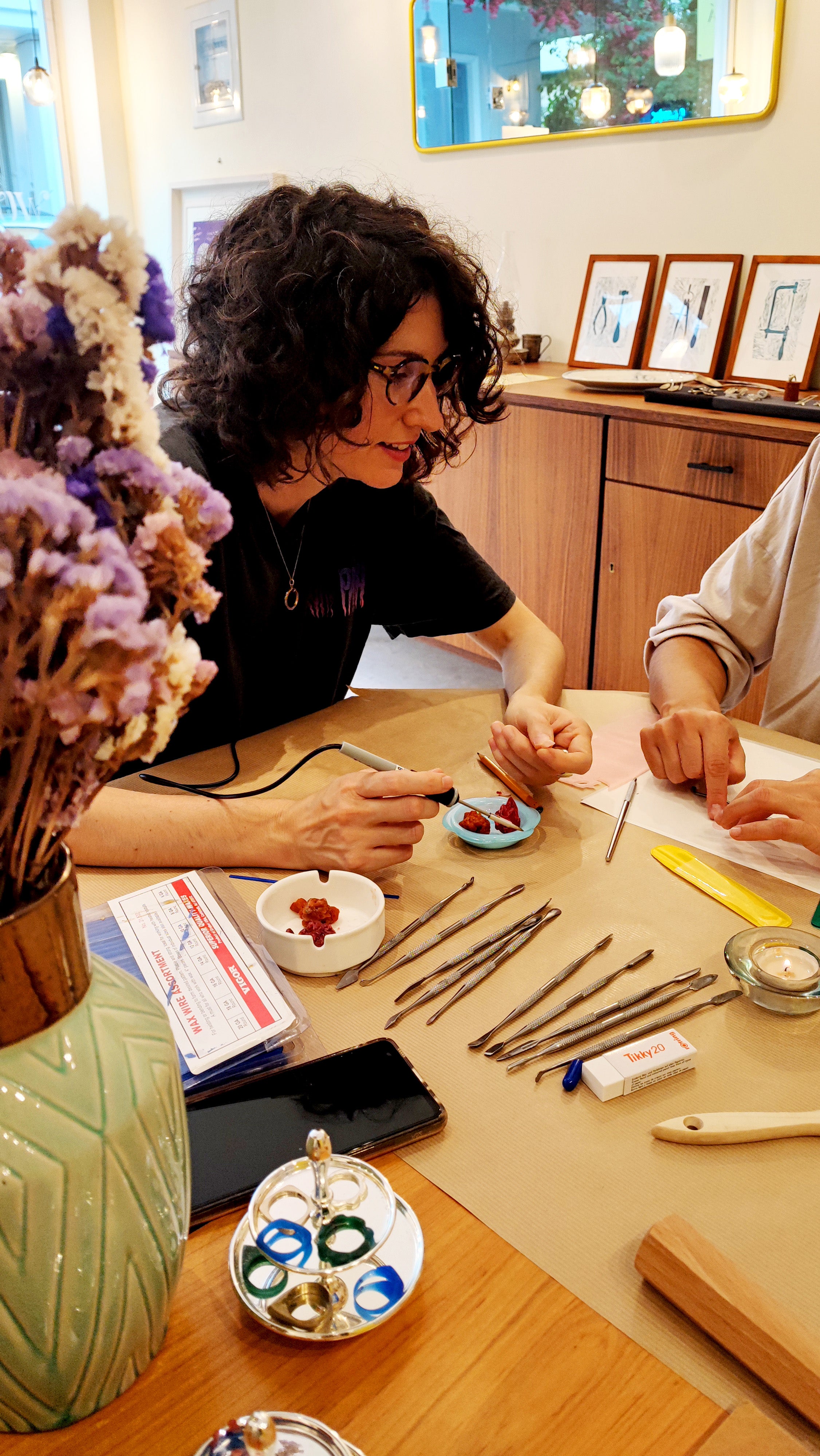 Two people working on a jewelry project at a table with various materials.