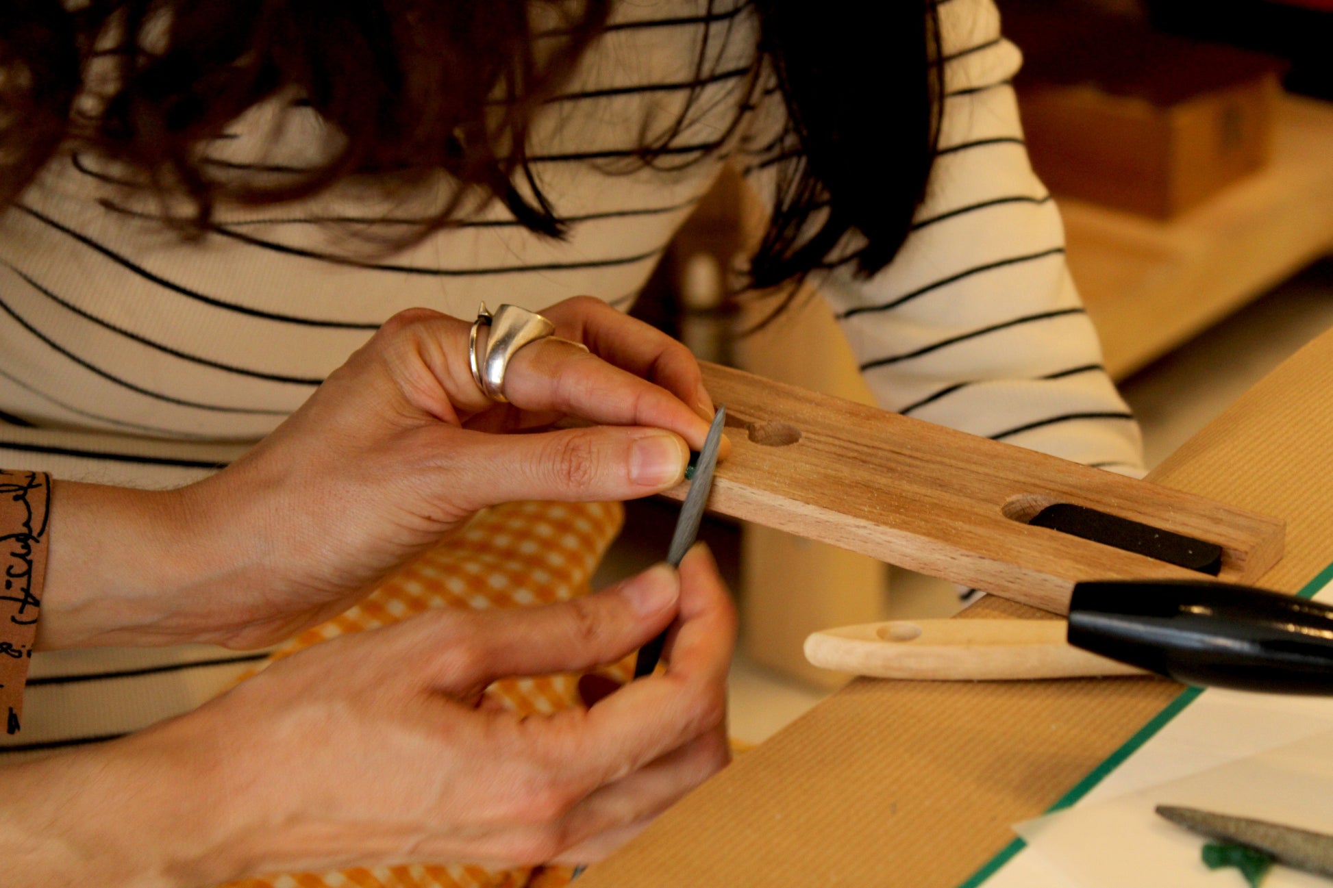 Close-up of hands working to create a pendant from a wax object with tools on a table.