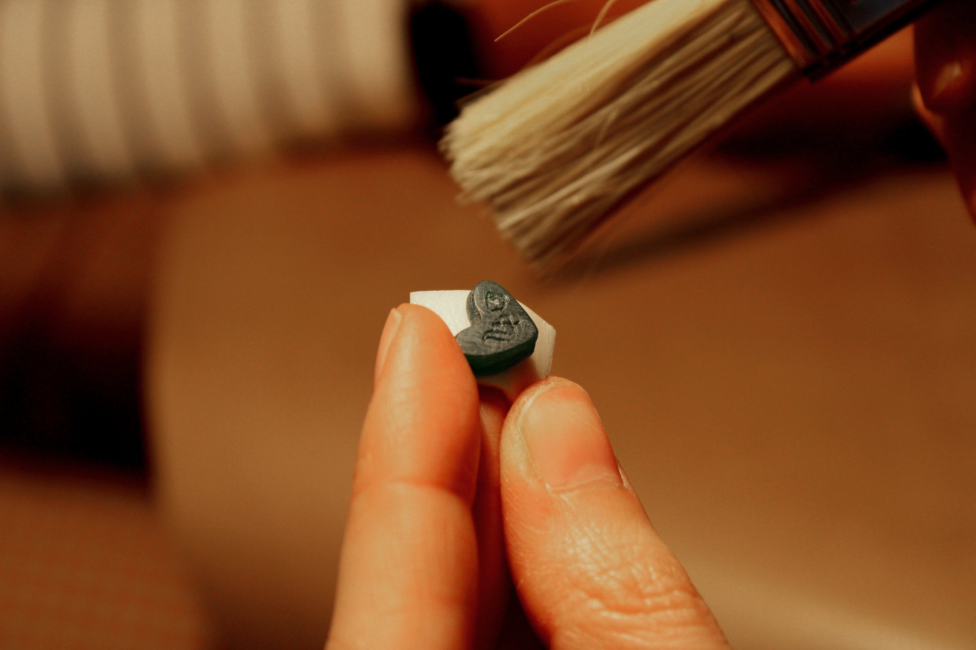 Hand holding a charm made of wax with a brush cleaning it