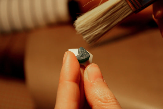 Hand holding a charm made of wax with a brush cleaning it