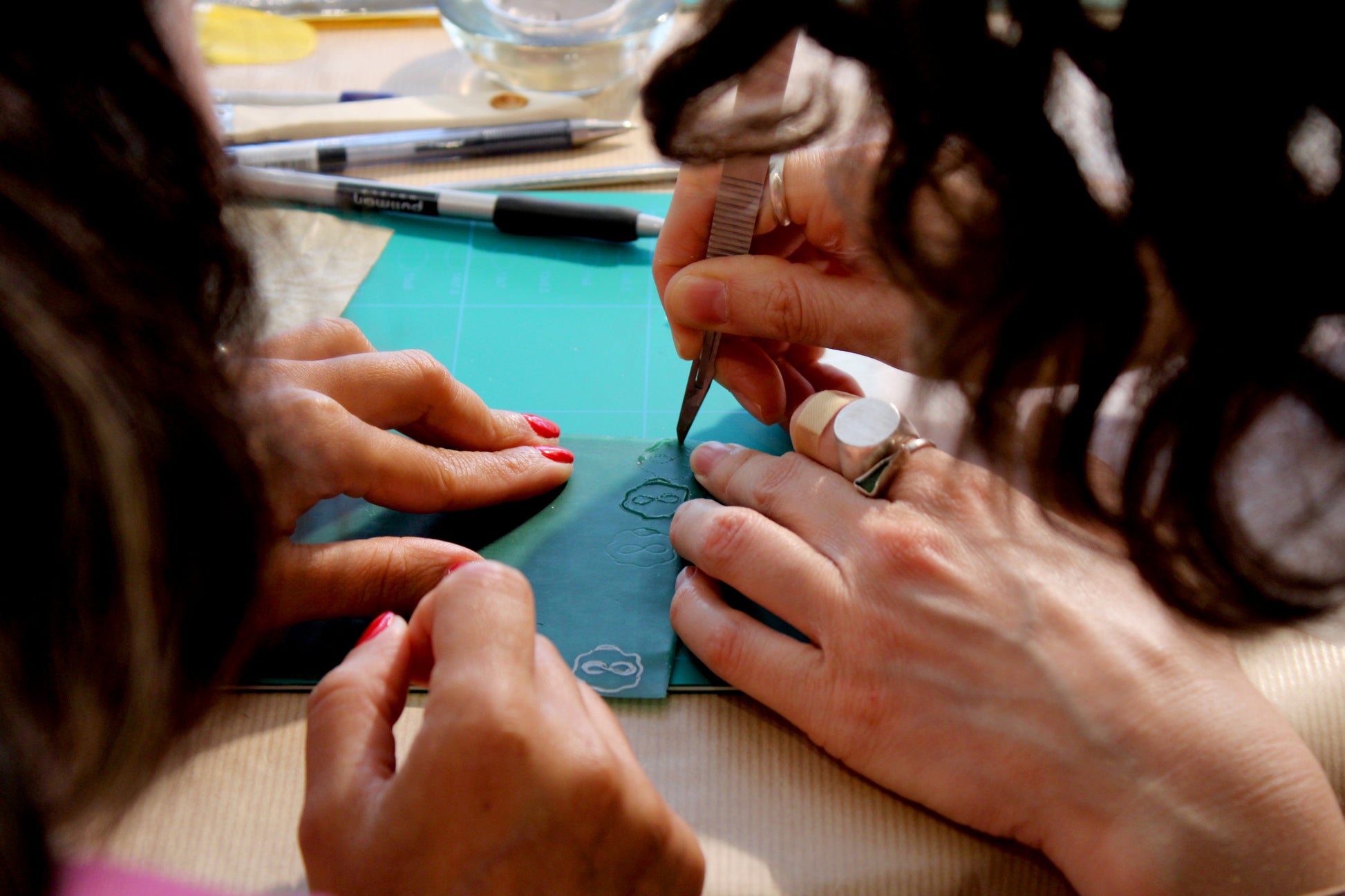 Close-up of hands using a small tool on a piece of thin wax with a green surface in the background.